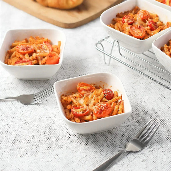 Bowls of pasta with tomatoes on a textured white surface with forks.