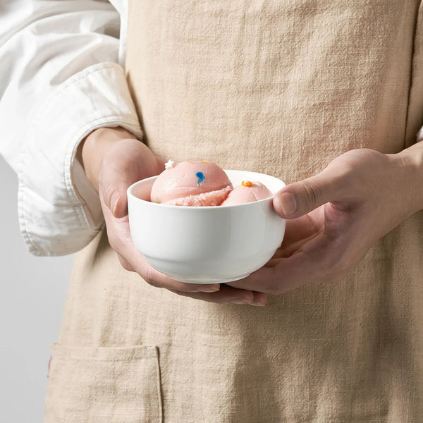 Person holding a white bowl with pink bath bombs against a neutral background