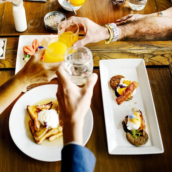 Two people toasting with glasses at a breakfast table with plates of food.