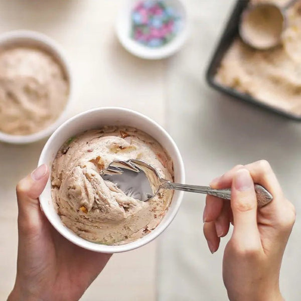 Person holding a bowl of ice cream with a spoon, with additional bowls of ice cream in the background.