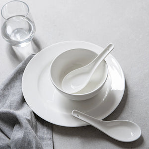 White ceramic bowl and spoons on a gray surface with a glass of water.