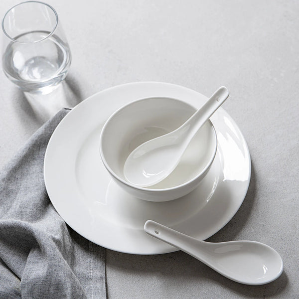 White ceramic bowl and spoons on a gray surface with a glass of water.