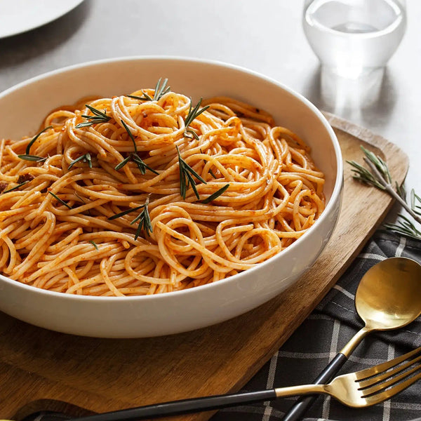 Bowl of spaghetti with rosemary on a wooden board with cutlery