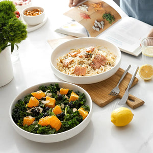 Two bowls of salad on a table with a book and lemon