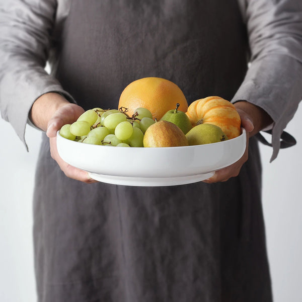 Person holding a bowl of fruit against a neutral background