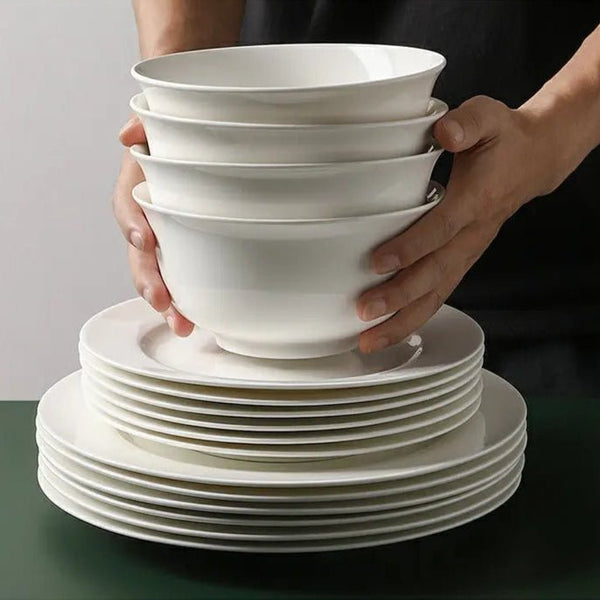 Stack of white ceramic bowls and plates held by a person against a neutral background