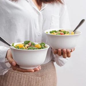 Person holding two bowls of salad with a plain background