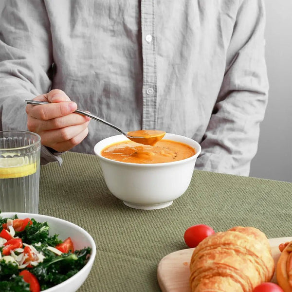 Person eating soup from a bowl with a side of salad and bread on a green tablecloth.