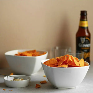 Two bowls of chips with a bottle of Guinness in the background on a neutral surface.