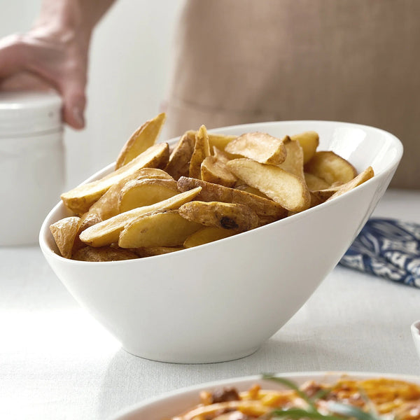 White bowl filled with potato wedges on a table.