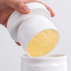 Hand pouring a yellow substance from a white container into another white container.