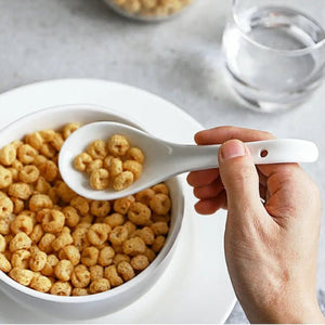 Hand holding a spoonful of cereal over a bowl with a glass of water in the background.