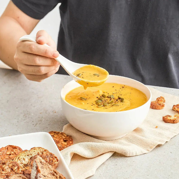 Person holding a spoon over a bowl of soup with crackers on the side