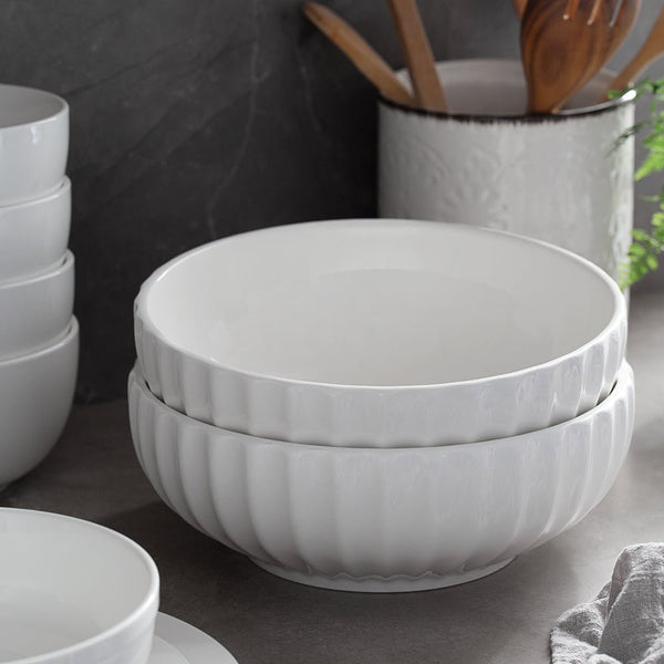 Stack of white ceramic bowls on a kitchen counter with utensils in the background.