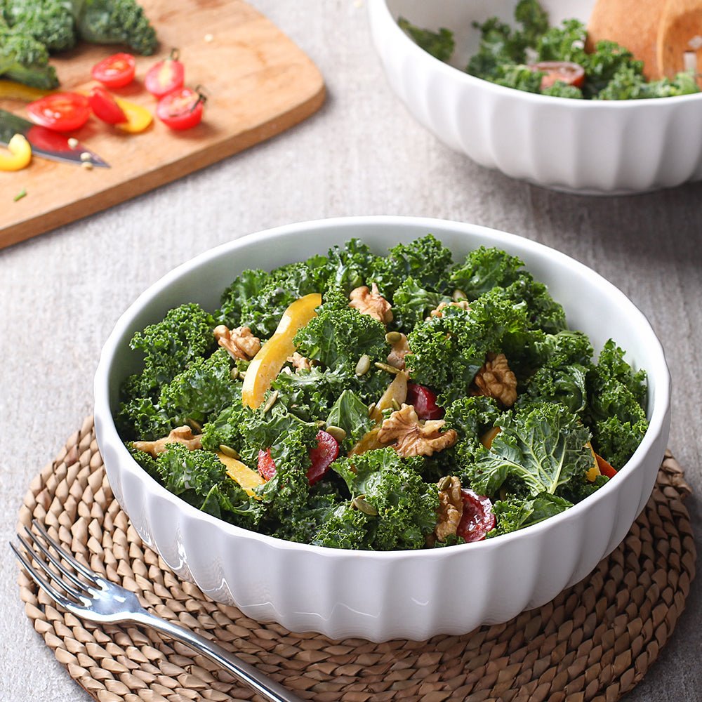 Kale salad with nuts and dried fruits in a white bowl on a textured surface.