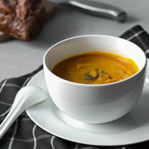White bowl of pumpkin soup on a gray surface with a black and white checkered napkin.