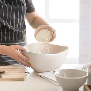 Person pouring rice from a small bowl into a larger white bowl on a kitchen counter.