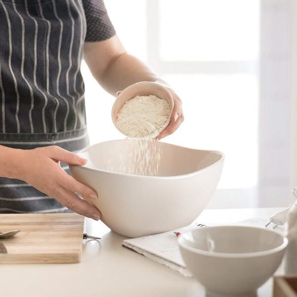Person pouring rice from a small bowl into a larger white bowl on a kitchen counter.