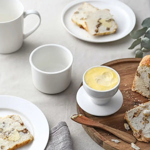 White ceramic items including cups and an egg cup on a table with bread and butter.