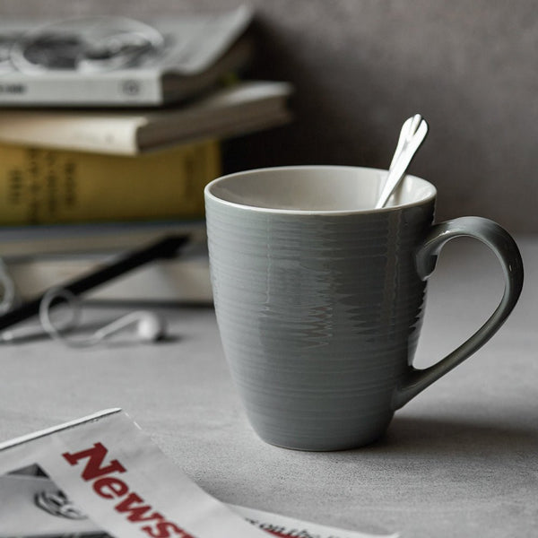 Gray mug with a spoon on a table with newspapers in the background