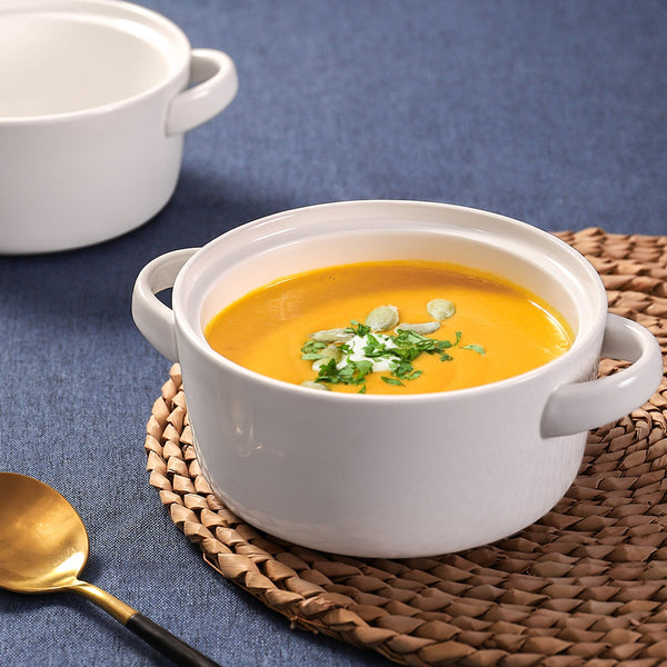 White bowl of yellow soup with garnish on a woven mat against a blue background