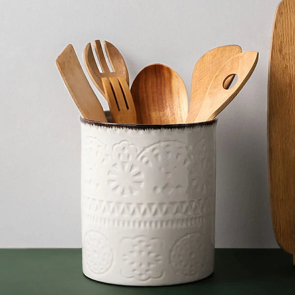 White ceramic utensil holder with wooden utensils against a neutral background