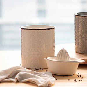 Two ceramic containers and a white juicer on a wooden surface with a blurred natural background