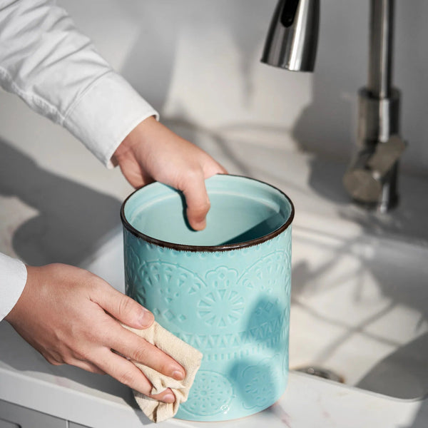 Person cleaning a blue ceramic cup with a cloth in a kitchen sink.