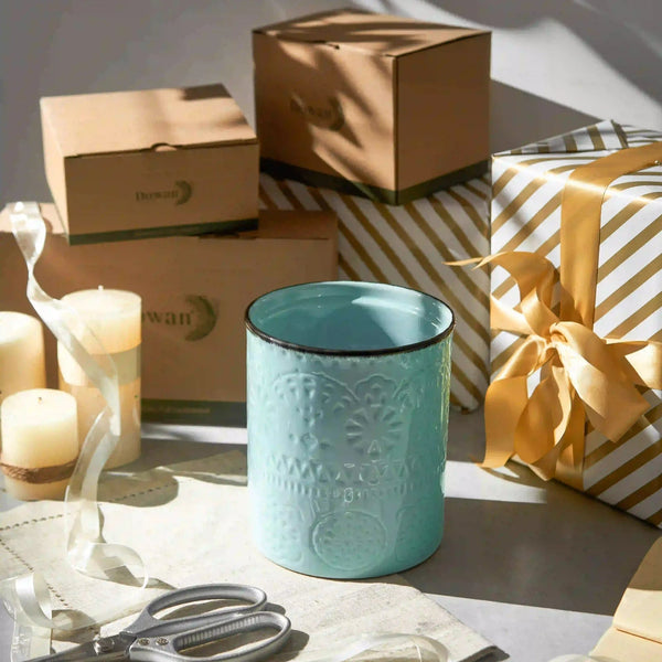 Teal ceramic mug with decorative patterns on a table with candles and gift boxes in the background
