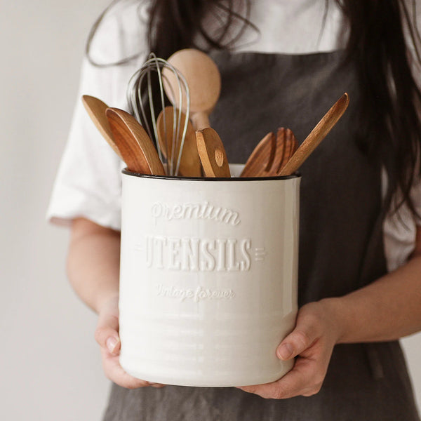 Person holding a container of wooden kitchen utensils with a neutral background
