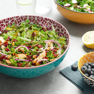 Salad in a decorative bowl on a table with a lemon and blueberries.