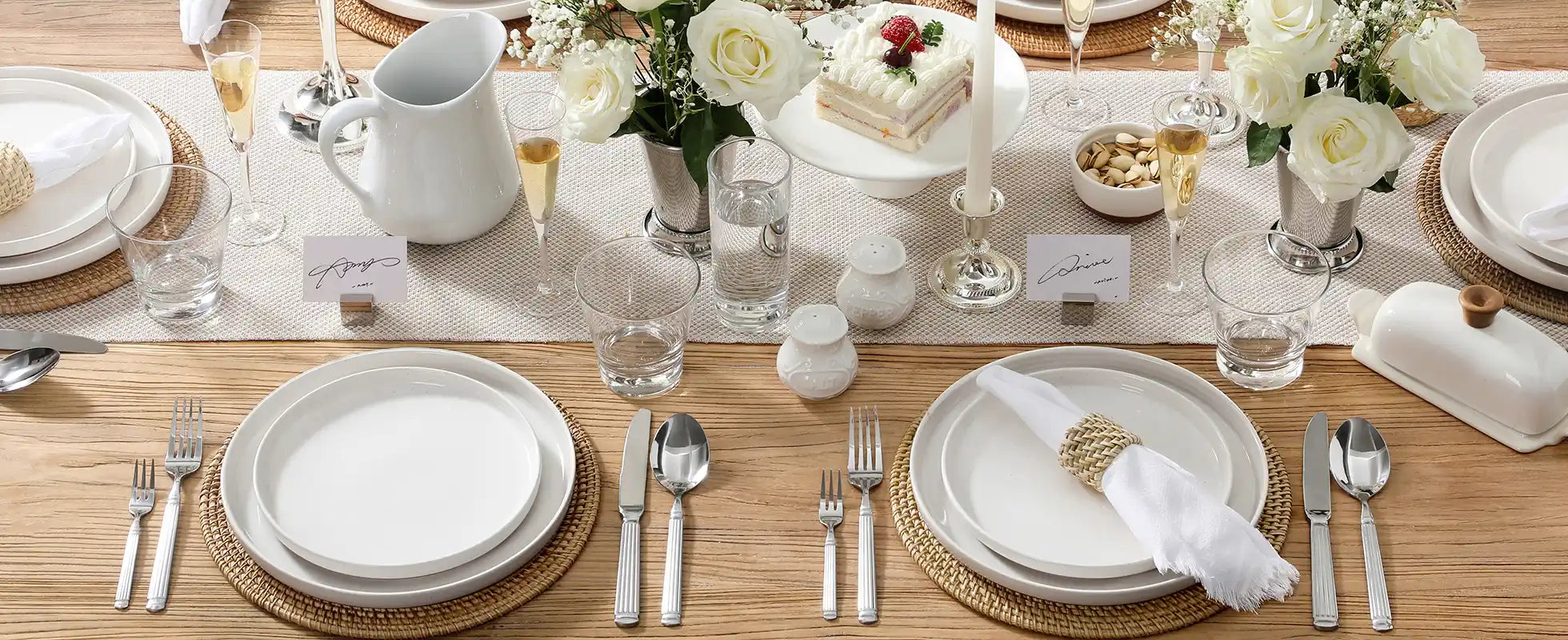 Elegant table setting with white dinner plates, silverware, and decorative elements on a wooden table.