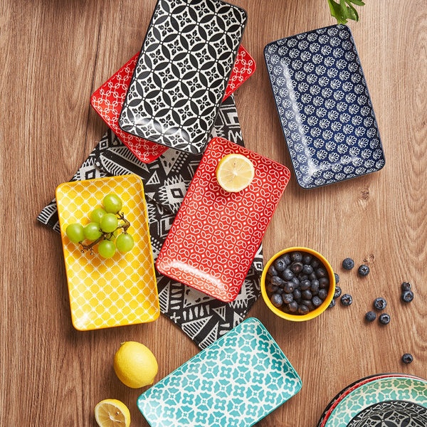 Colorful patterned ceramic trays on a wooden surface with fruits and berries.
