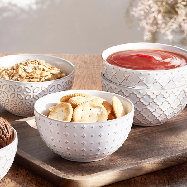 Set of white patterned bowls containing snacks on a wooden surface.