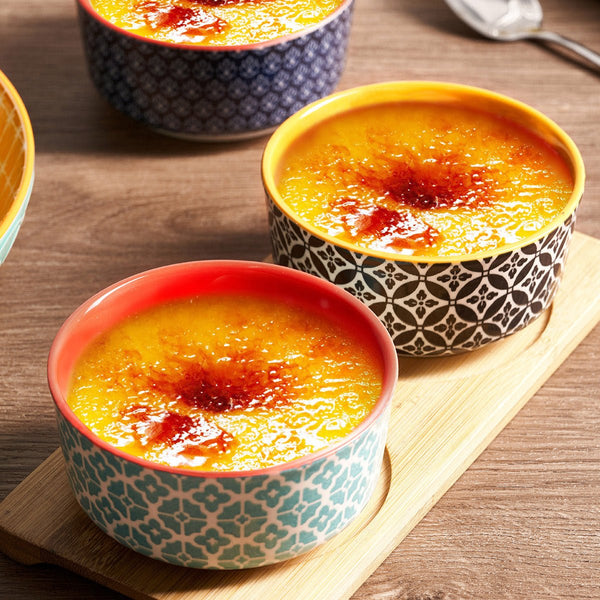 Three bowls of crème bréleé on a wooden board with a wooden background.