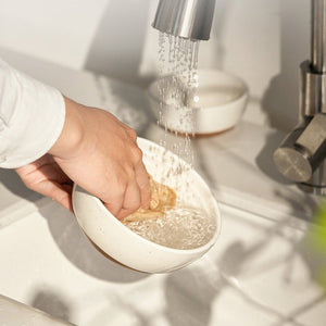 Person washing a bowl under running water in a kitchen sink.