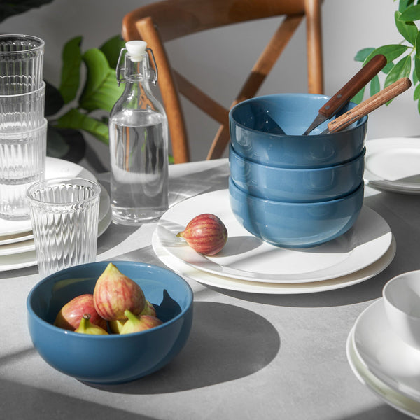 Blue ceramic bowls on a table with glasses, a bottle, and fruit.