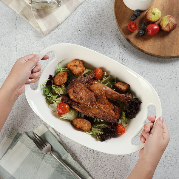 White oval platter with roasted chicken and vegetables on a light gray surface.