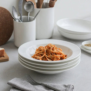 White ceramic bowls with spaghetti on a light gray surface, surrounded by kitchen utensils.