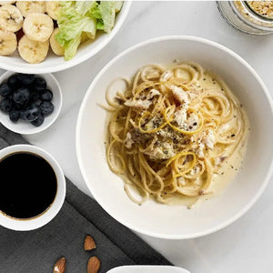Bowl of pasta with a side of salad, fruit, and coffee on a table.