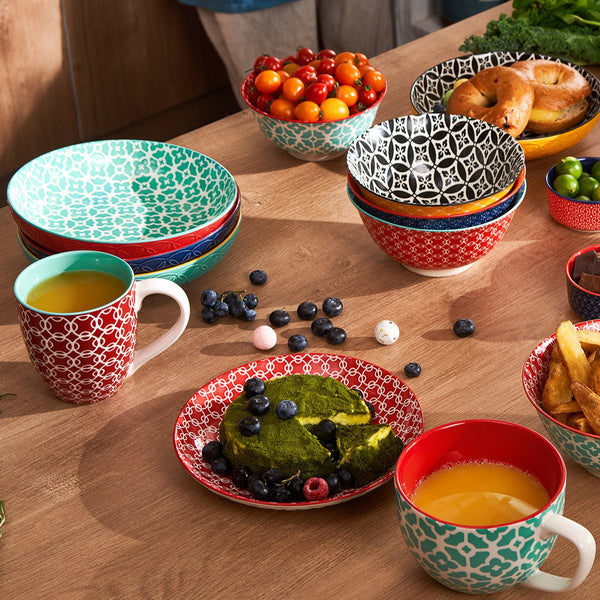 Colorful ceramic dishes and mugs on a wooden table with food.