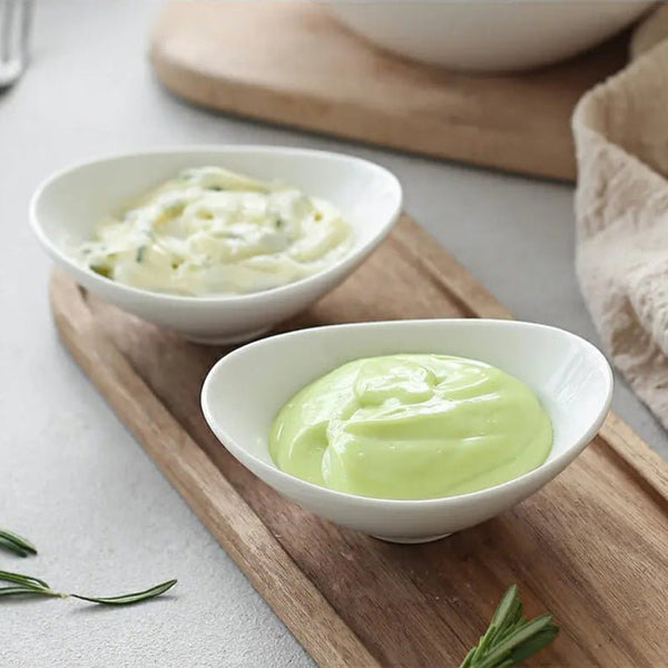 Two white bowls with green and white substances on a wooden board.