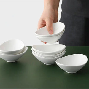 White ceramic bowls stacked on a green surface with a person's hand reaching for one.