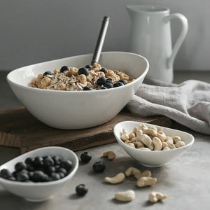 White bowl of granola with blueberries and a smaller bowl of nuts on a wooden surface.