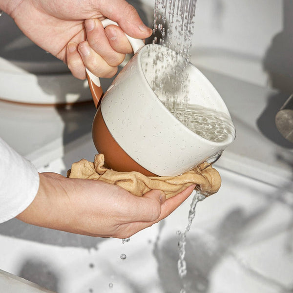 Person washing a 18 oz coffee mug with water and a cloth under running water.