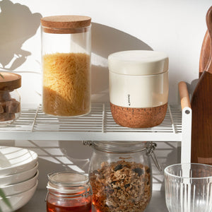 Kitchen shelves with jars containing food items and a white container with cork base.
