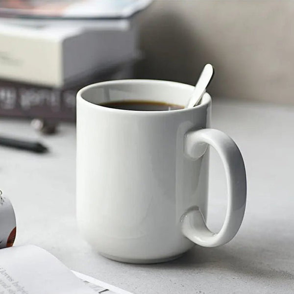 White mug with a spoon in black coffee on a light surface