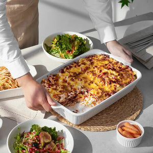 Person serving a dish of cheesy casserole with salads and carrots on a table.