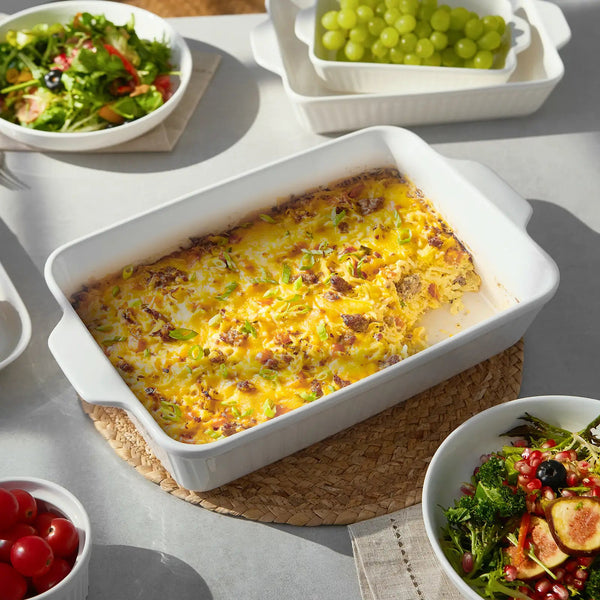 Baked dish in a white casserole dish with salads and grapes on a table