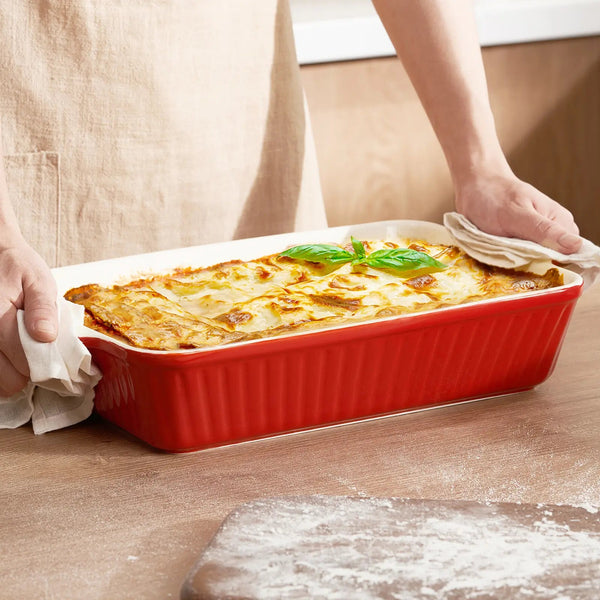 Person holding a red baking dish with lasagna on a wooden surface